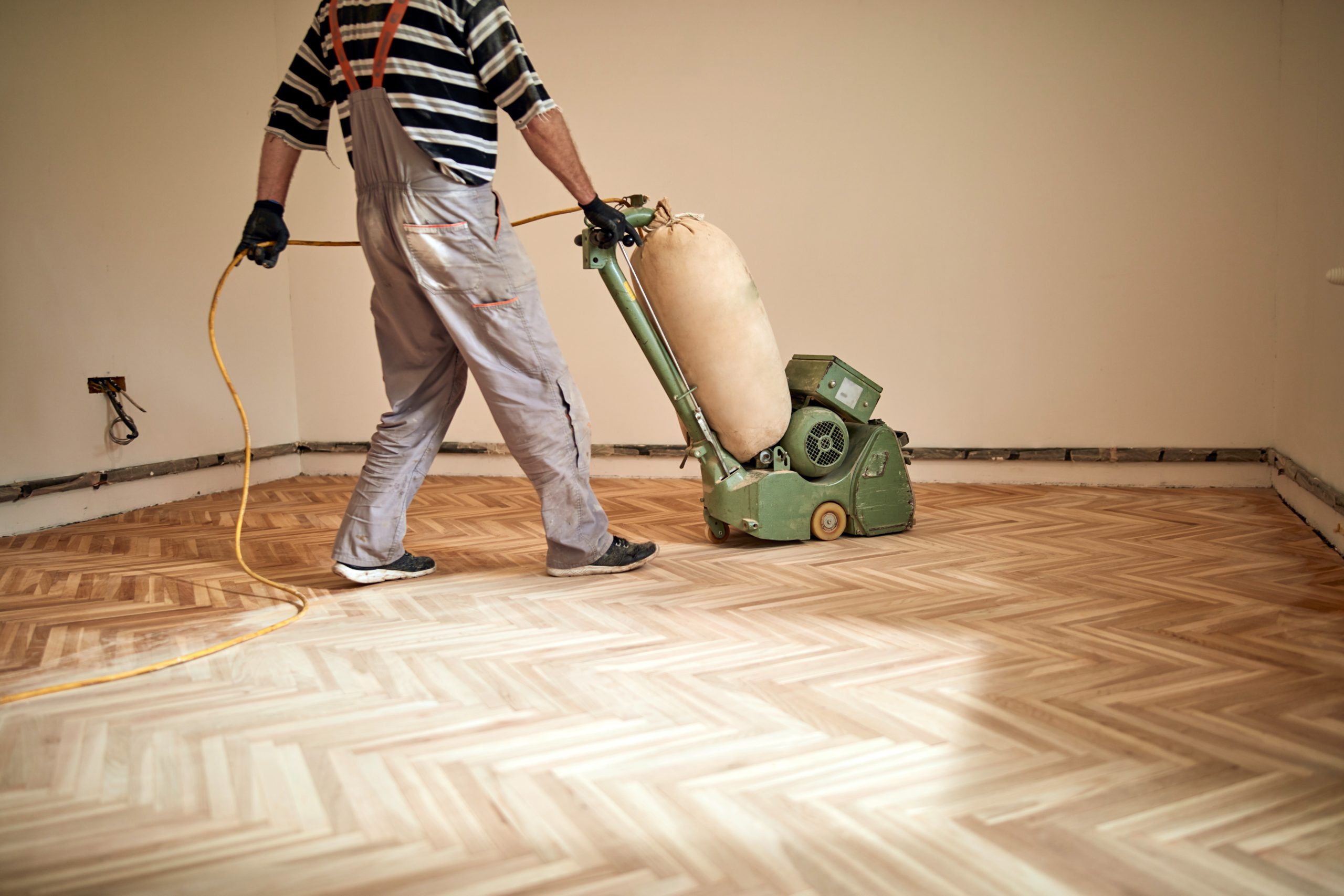 Sanding Parquet Floors in Sydenham – tradesperson using a belt sander on a herringbone oak parquet floor, levelling the surface for refinishing.