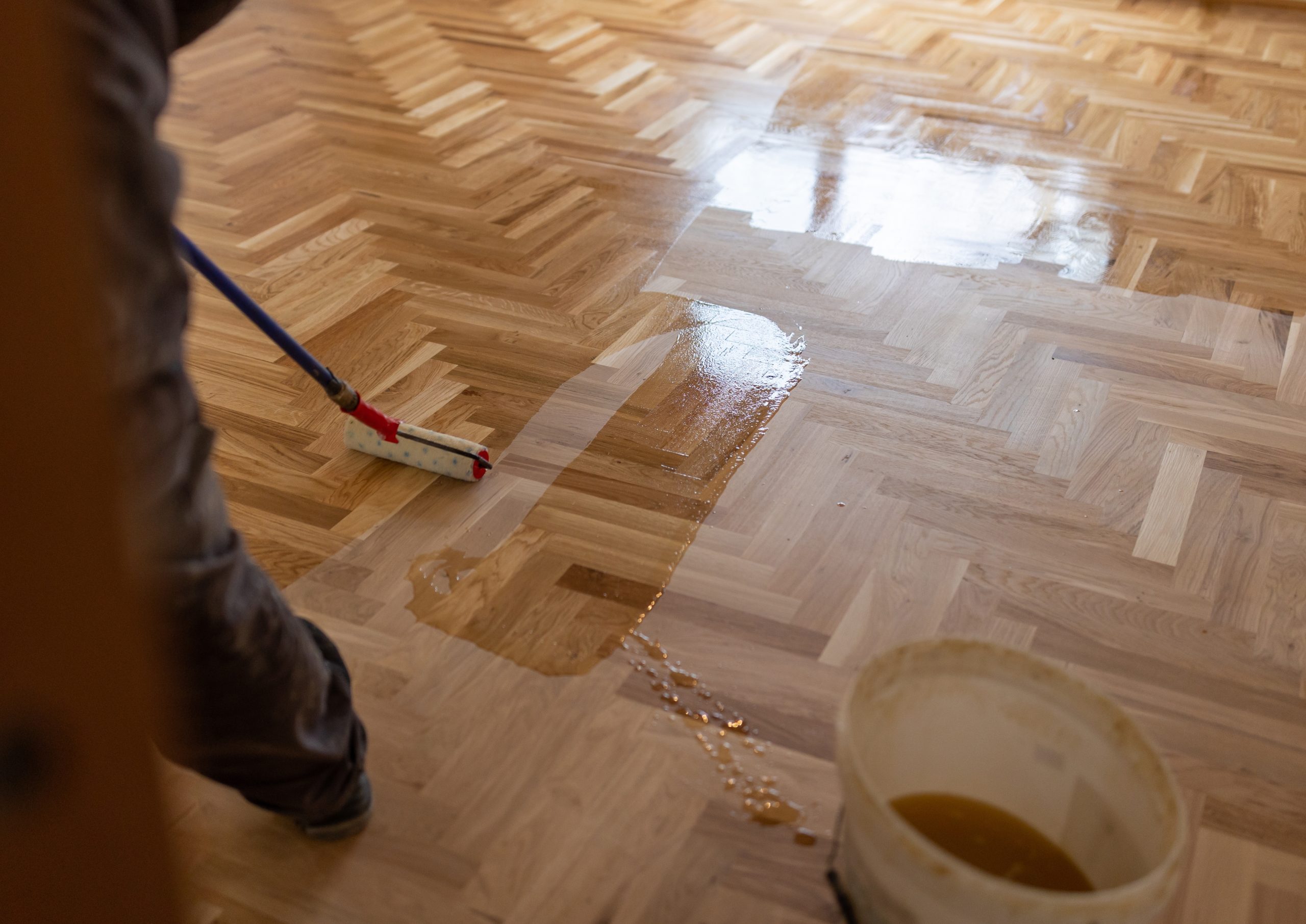 Sanding Parquet Floors in Sydenham – technician rolling a clear lacquer across a freshly sanded herringbone oak parquet floor, creating an even wet edge.