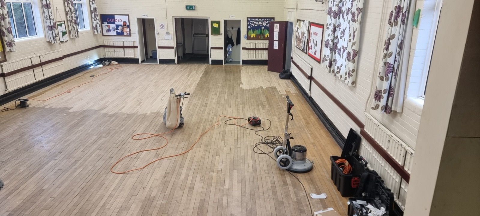 Wood Floor Sanding in Sydenham on a maple hardwood strip school hall floor, showing the central area being sanded with professional machines while darker, unsanded sections remain around the edges.