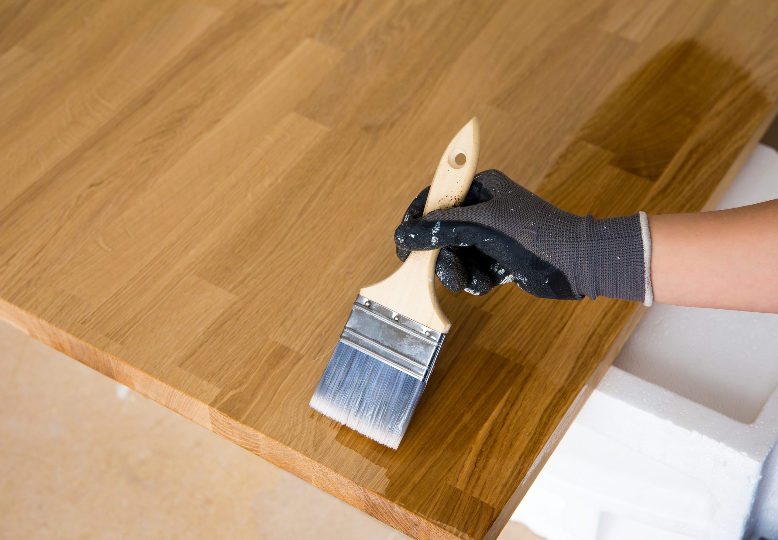 Wood Floor Sanding in Sydenham applied finish on a solid oak hardwood surface, with a gloved hand brushing protective coat onto an oak worktop-style board.