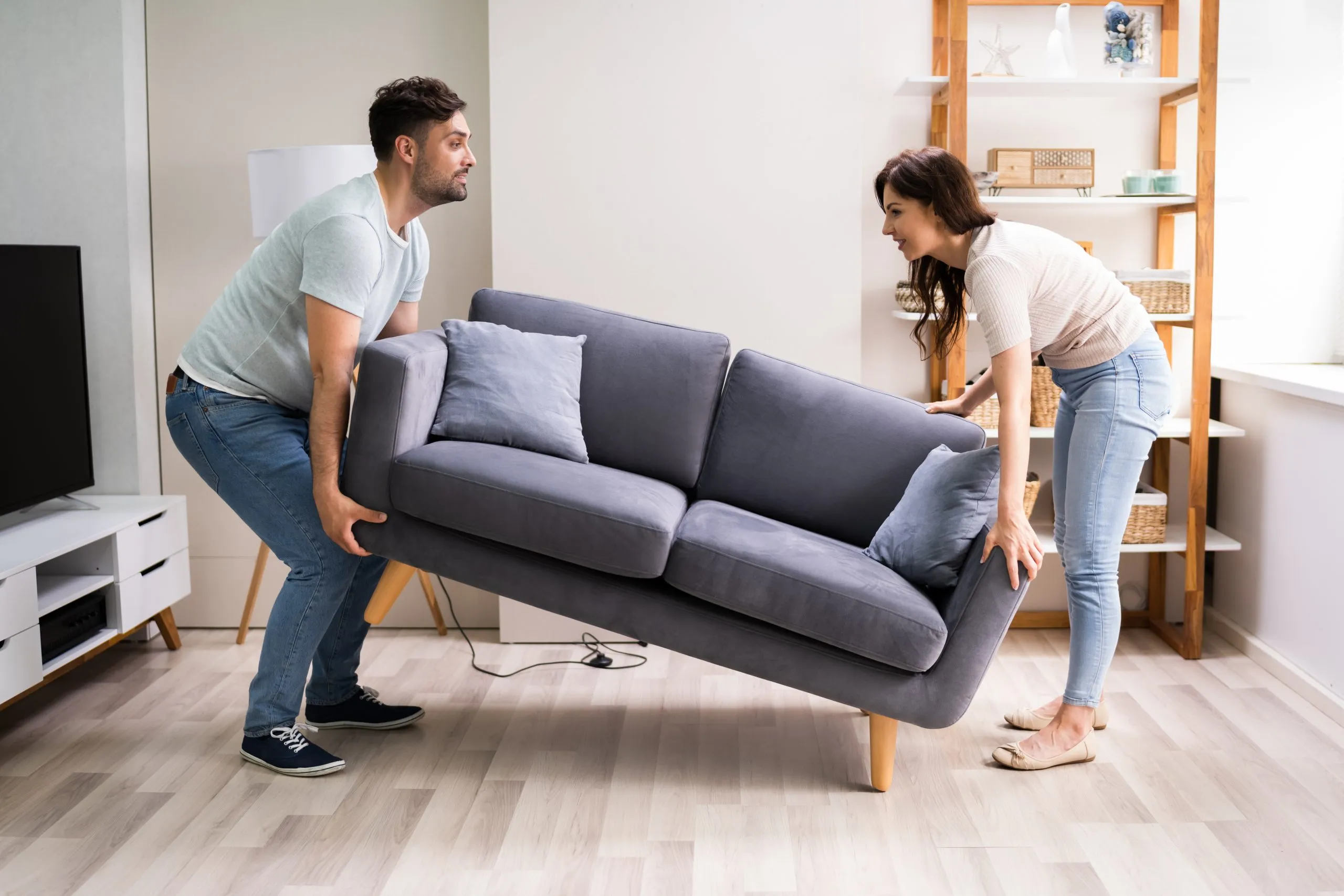 Hardwood Floor Refinishing in Sydenham with a couple lifting a sofa off a light oak engineered hardwood living room floor to prepare the space for refinishing.