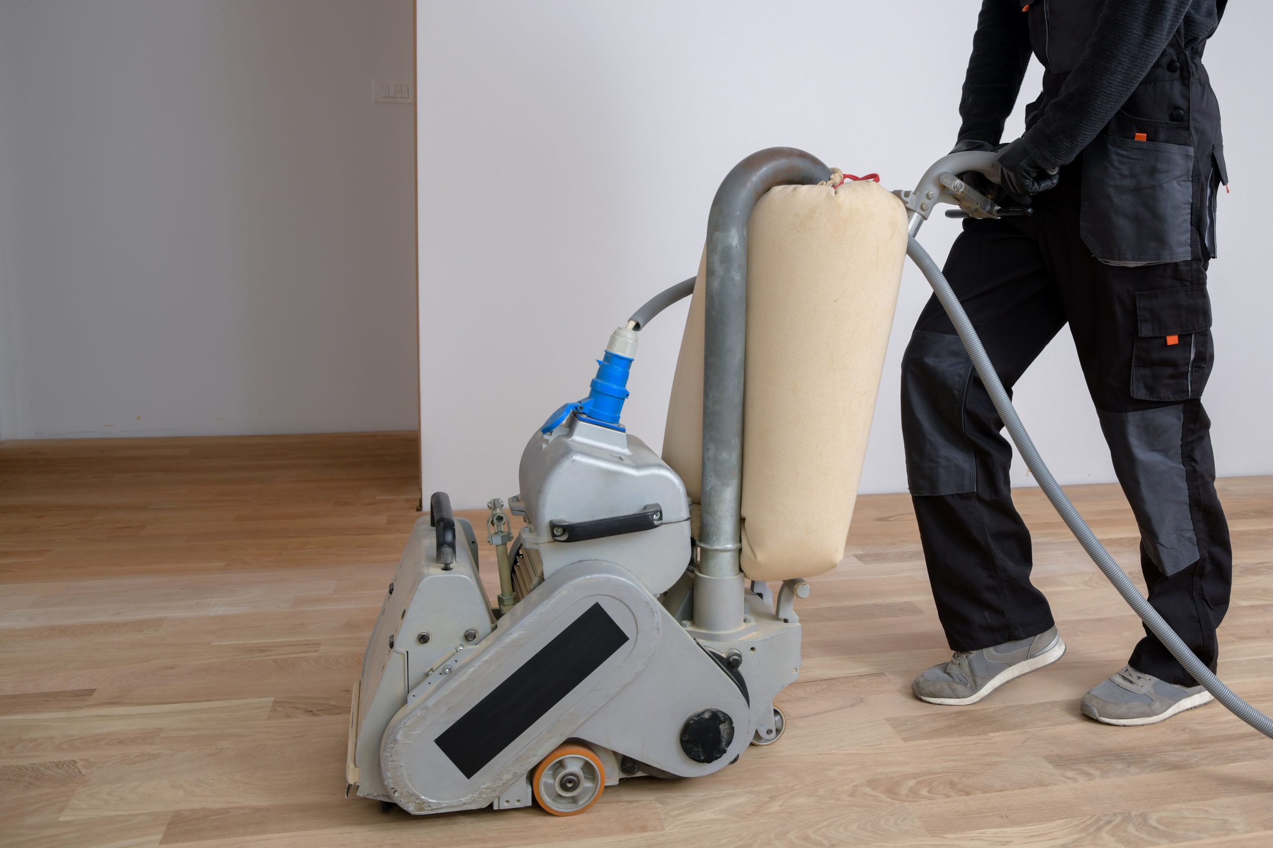 Hardwood Floor Refinishing in Sydenham with a technician using a belt sander on a light oak hardwood plank floor to prepare it for new finish.