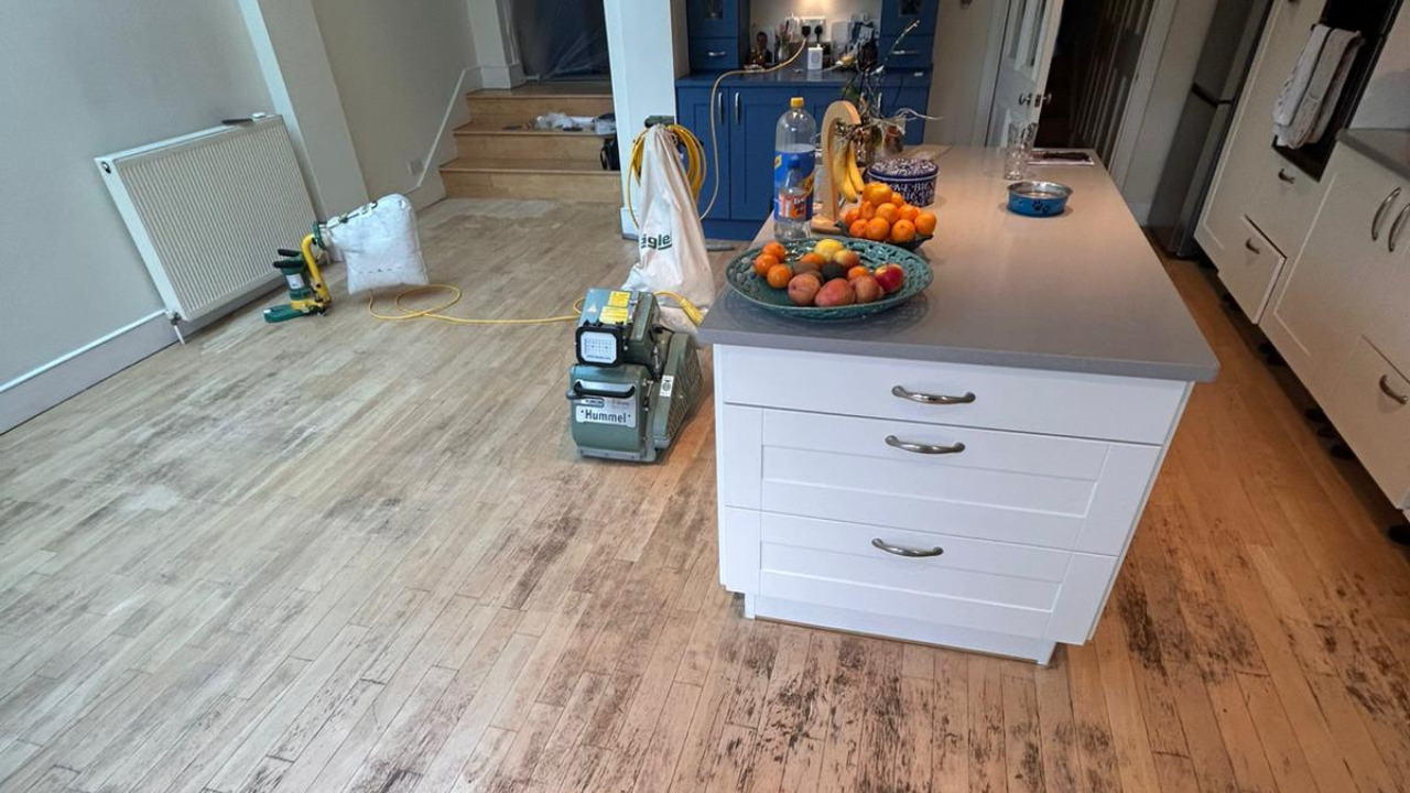 Hardwood Floor Refinishing in Sydenham showing a worn oak strip hardwood kitchen floor mid-sanding, with professional sanding machines set up around the island.