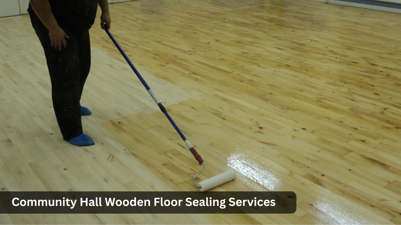 Worker applying clear sealant with a roller to a freshly sanded wooden floor in a community hall, showing the glossy wet finish next to the natural timber